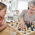 Una niña enseña a jugar al ajedrez a su abuela.