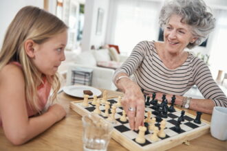 Una niña enseña a jugar al ajedrez a su abuela.
