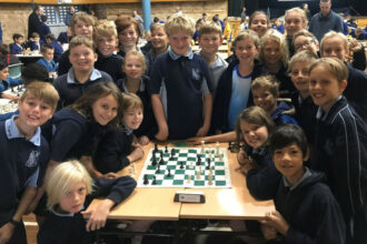 Grupo de niños sonríe a la cámara en una competición de ajedrez.
